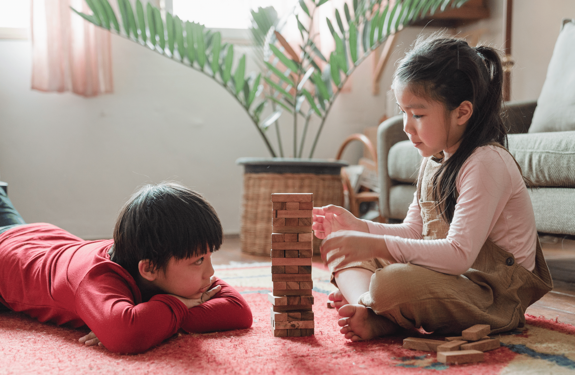 Boy and girl sit on the floor building a tower from wooden blocks